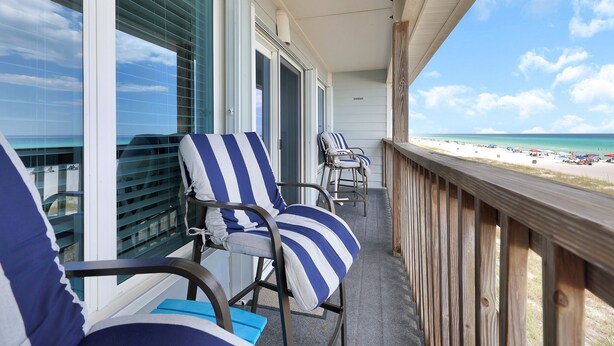 A balcony with striped chairs and a view of the beach.