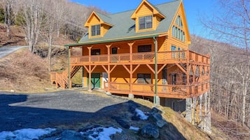 Situated in a mountainous area, this cabin features a front porch and a staircase leading to the upper level.