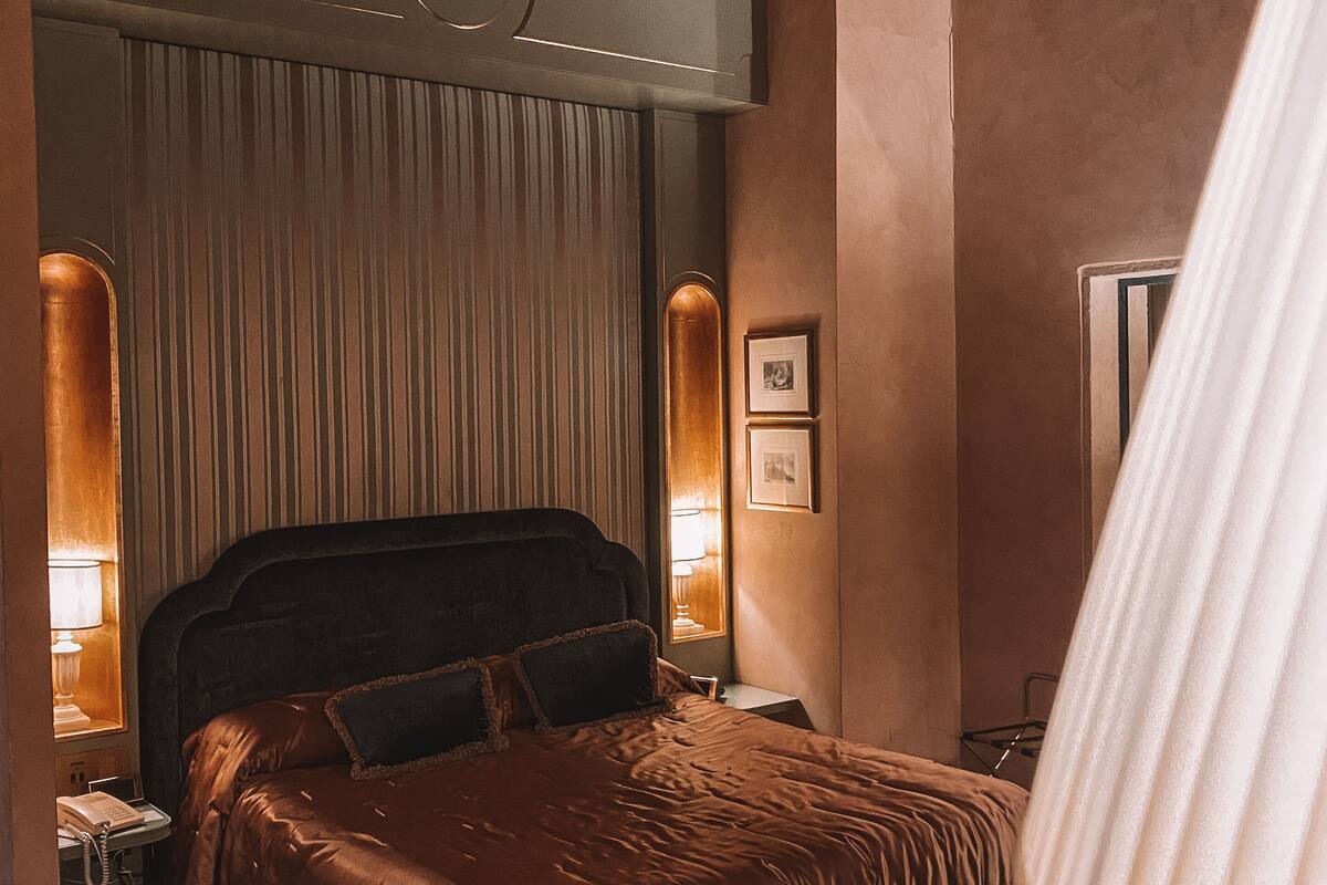 A bedroom with a large bed, a nightstand with a lamp, and a wardrobe.