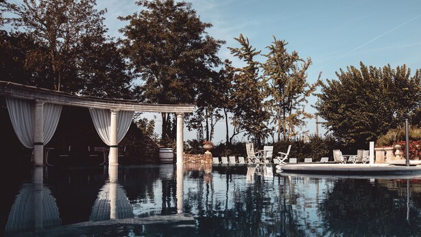 A serene pool area with a pergola, lounge chairs, and a clear reflection in the water. - Relais Villabella (San Bonifacio)