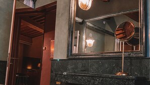 A bathroom with a dark marble countertop, a round stool, a large mirror, and a hanging light fixture. - Relais Villabella (San Bonifacio)