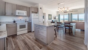 Una cocina moderna con una isla central, electrodomésticos integrados y una zona de comedor con vista al océano.