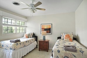A bedroom with two single beds, a ceiling fan, a nightstand with a lamp, and a framed picture on the wall.