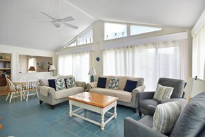 A spacious living room with a ceiling fan, two sofas, a coffee table, and a dining area with chairs.