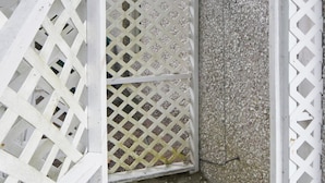 Un área de ducha de concreto con una puerta blanca de celosía, rodeada por una estructura de celosía blanca.