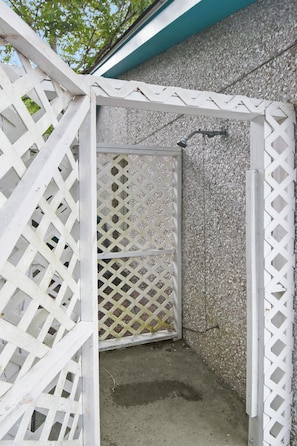 A concrete shower area with a white lattice door, surrounded by a white lattice structure.