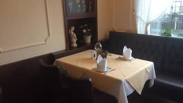 A dining area with a table set for two, a vase with flowers, and a window with curtains.