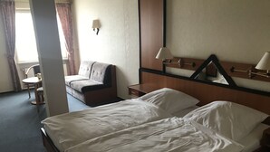 Una habitación de hotel con cama, sofá, sillón, mesa y lámpara.