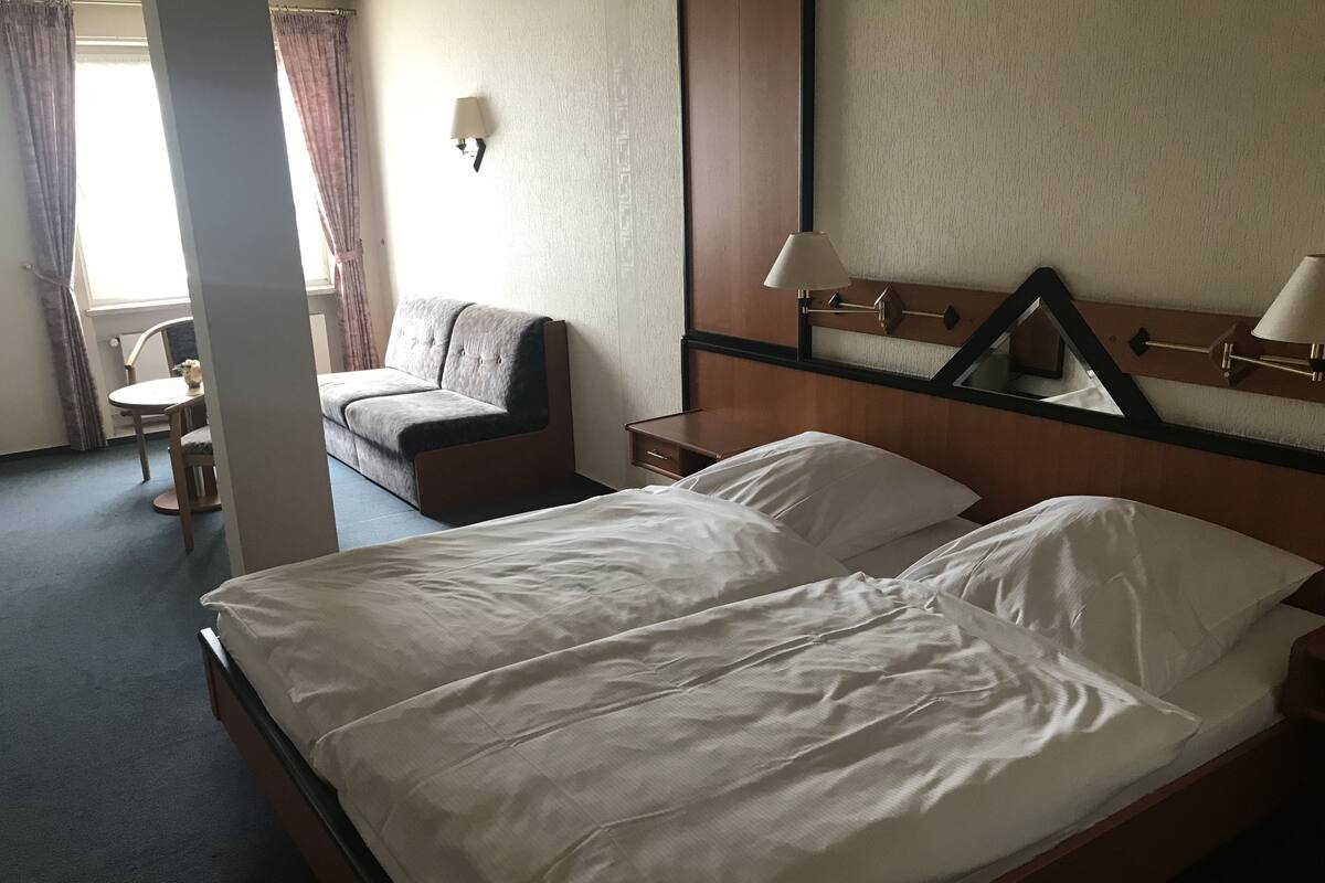 A hotel room with a bed, a sofa, a chair, a table, and a lamp.