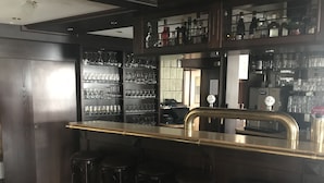 Una zona de bar con mostrador, taburetes y estanterías llenas de copas.