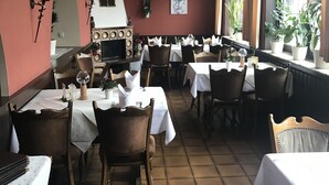 Un restaurante con varias mesas y sillas, suelo de baldosas y una pared roja con un arco blanco.