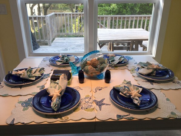 A dining table set with blue plates and napkins, a decorative glass bowl, and a candle. - All Decked Out -OBX MP6 (Kill Devil Hills)