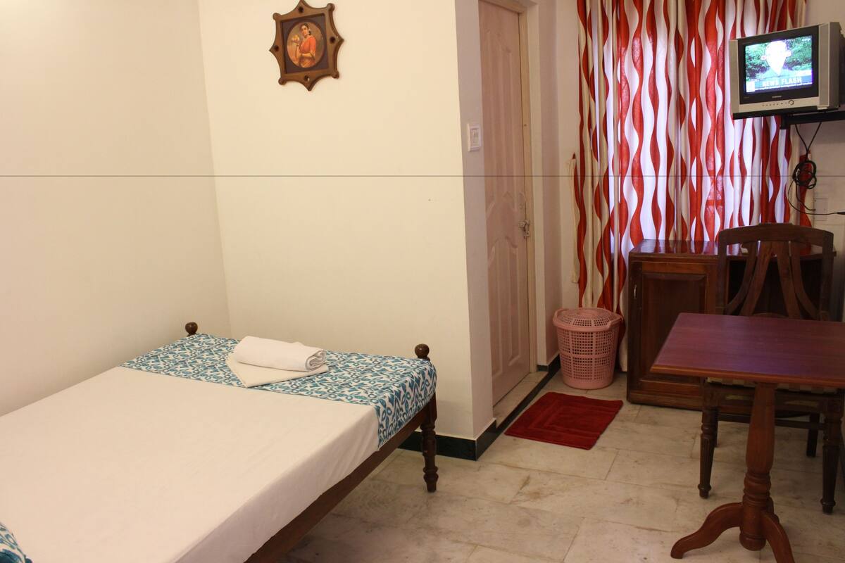 A small room with a single bed, a wooden chair, a television, and a door with a striped curtain.