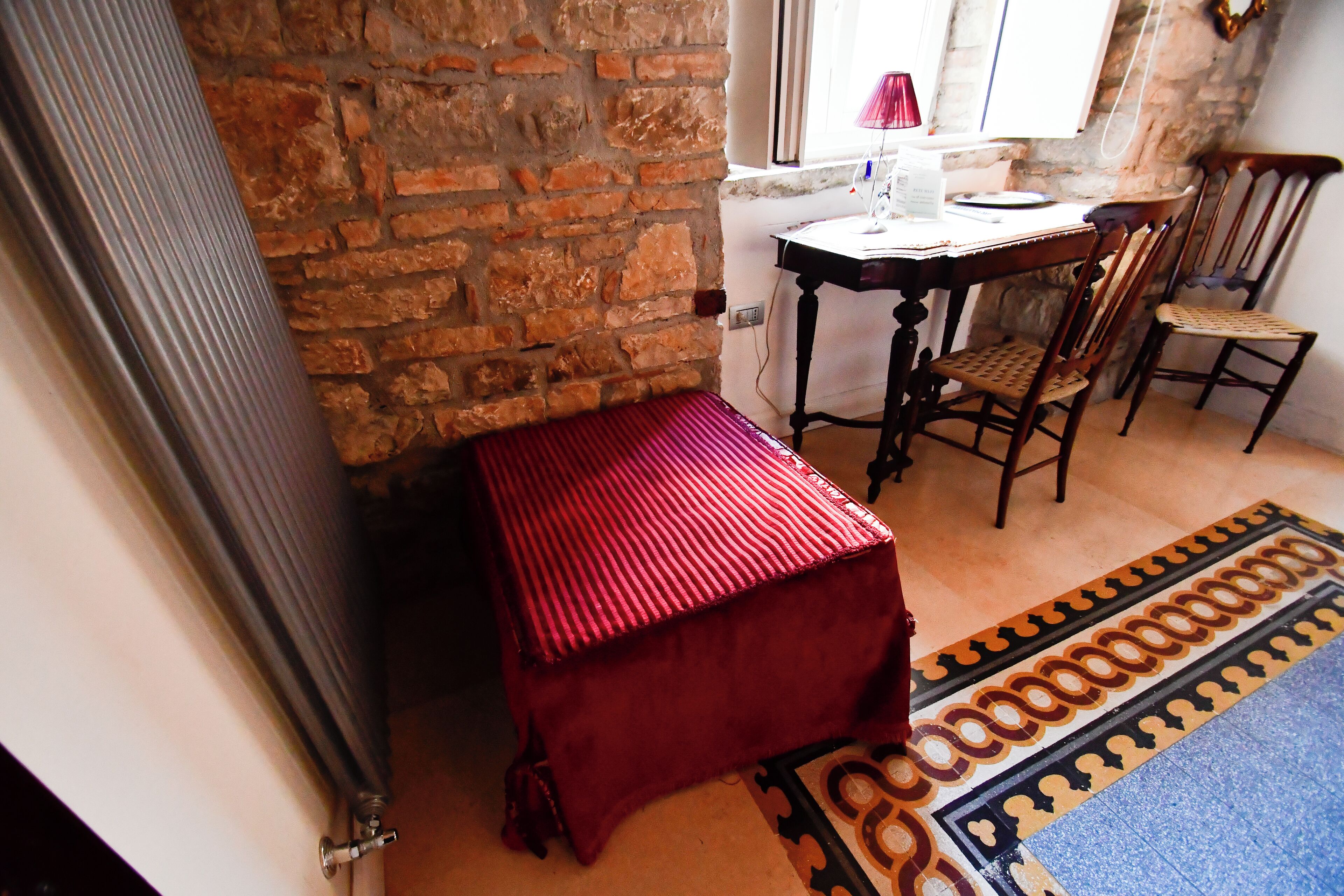 A room with a brick wall, a wooden table, a red bench, and patterned flooring.