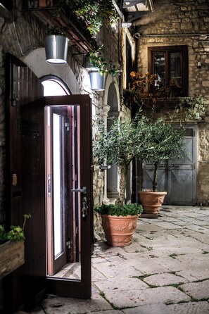 An open wooden door leading into a stone building with a potted olive tree and a large terracotta pot. - Guest House Al Convento (Potenza)