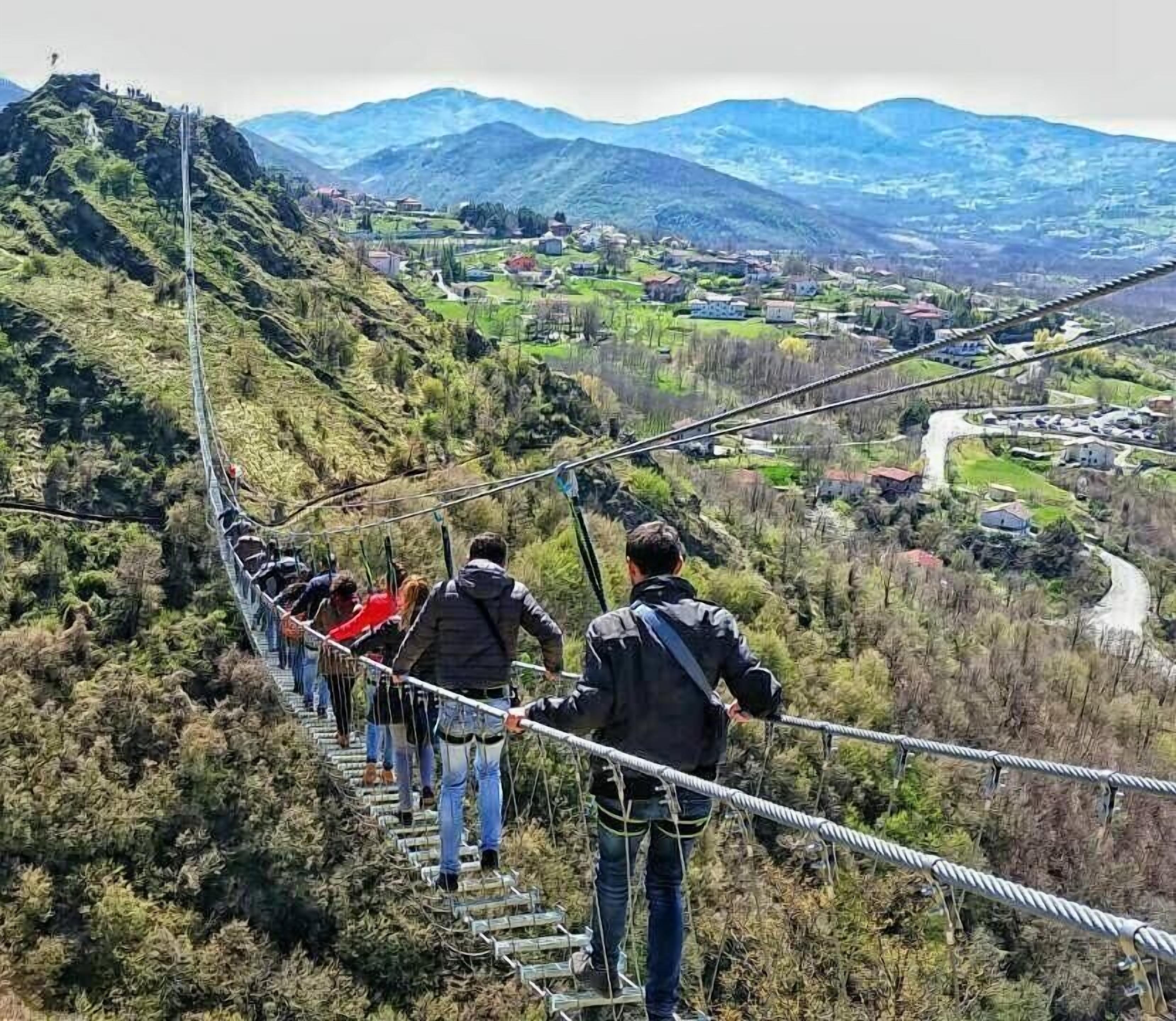A group of people on a suspension bridge with a mountainous landscape in the background.