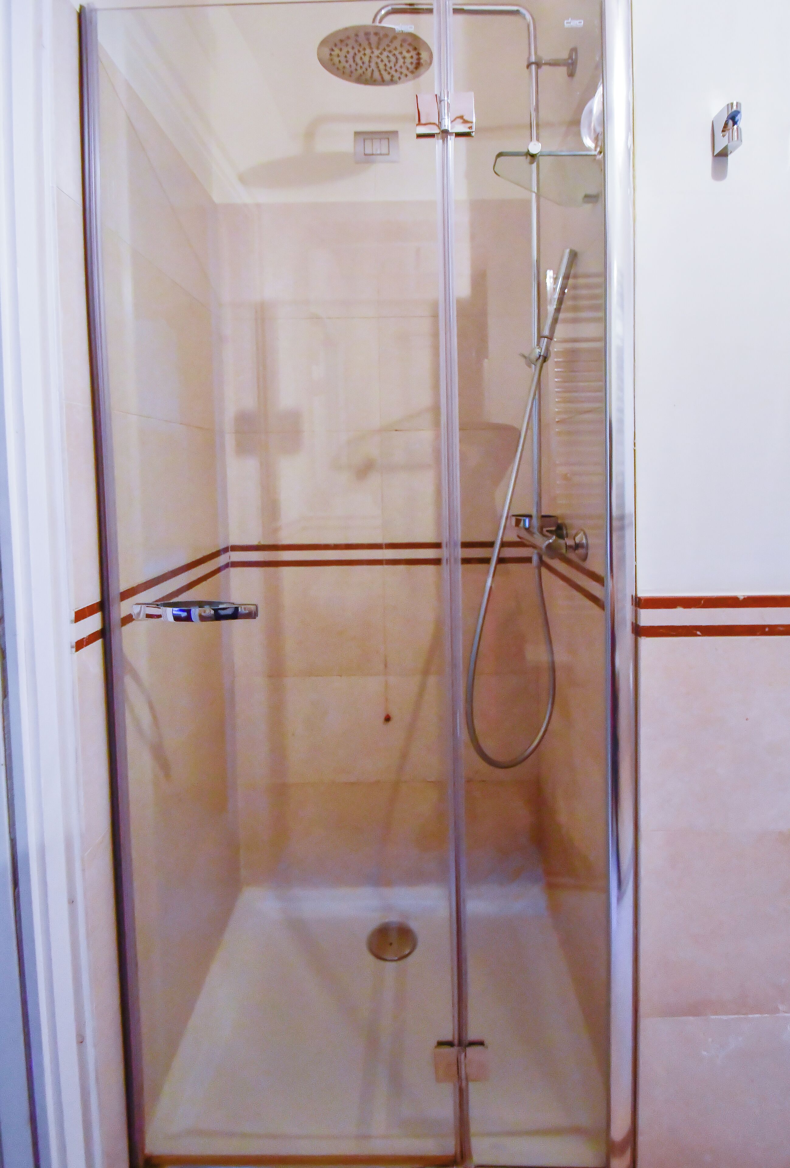 Una cabina de ducha con paredes de vidrio, un cabezal de ducha manual, un grifo instalado en la pared y un desagüe.