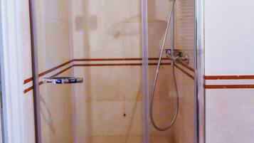 Una cabina de ducha con paredes de vidrio, un cabezal de ducha manual, un grifo instalado en la pared y un desagüe.