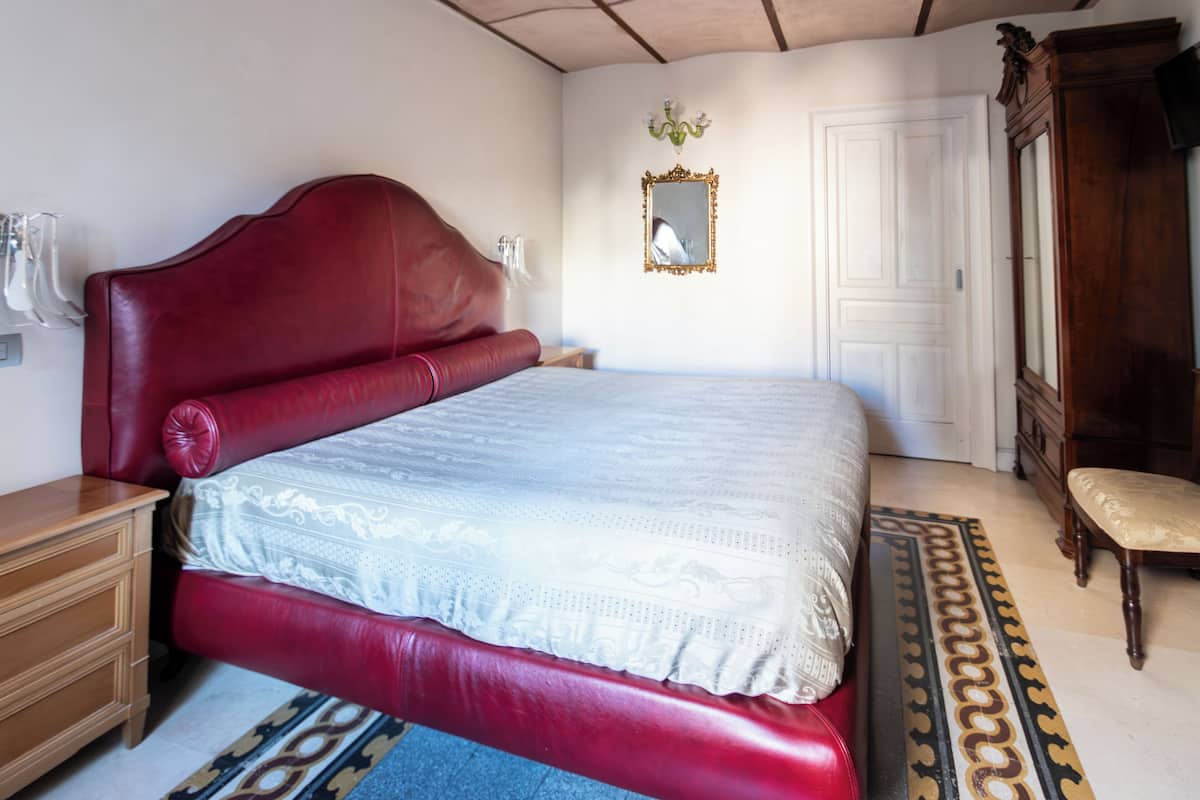 A bedroom with a red bed, a wooden dresser, a mirror, and a door.