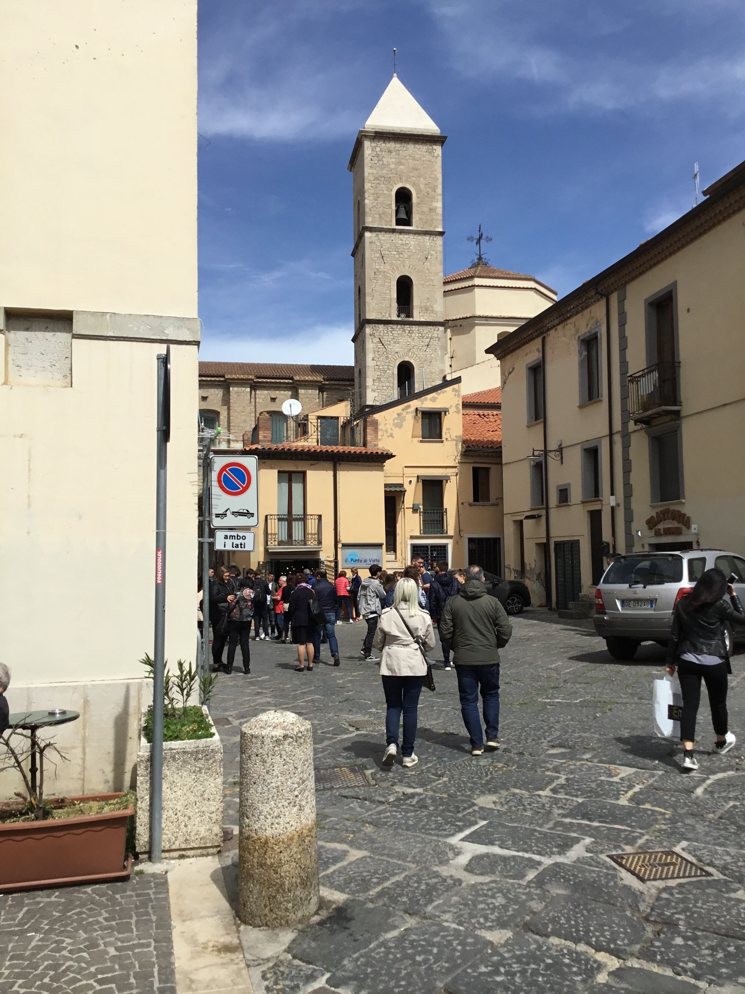 Una calle empedrada con edificios históricos, una torre de campanas y una señal de 'no estacionar'.