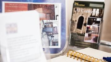 Una mesa de vidrio con un cuaderno, un folleto y un cartel para el B&B AI Convento, premio 2015.