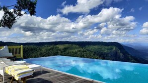 An infinity pool with wooden decking, lounge chairs, and towels. - Hills & Hues (Peermade)