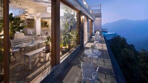 An outdoor terrace with seating and potted plants, overlooking a mountainous landscape. - Hills & Hues (Peermade)