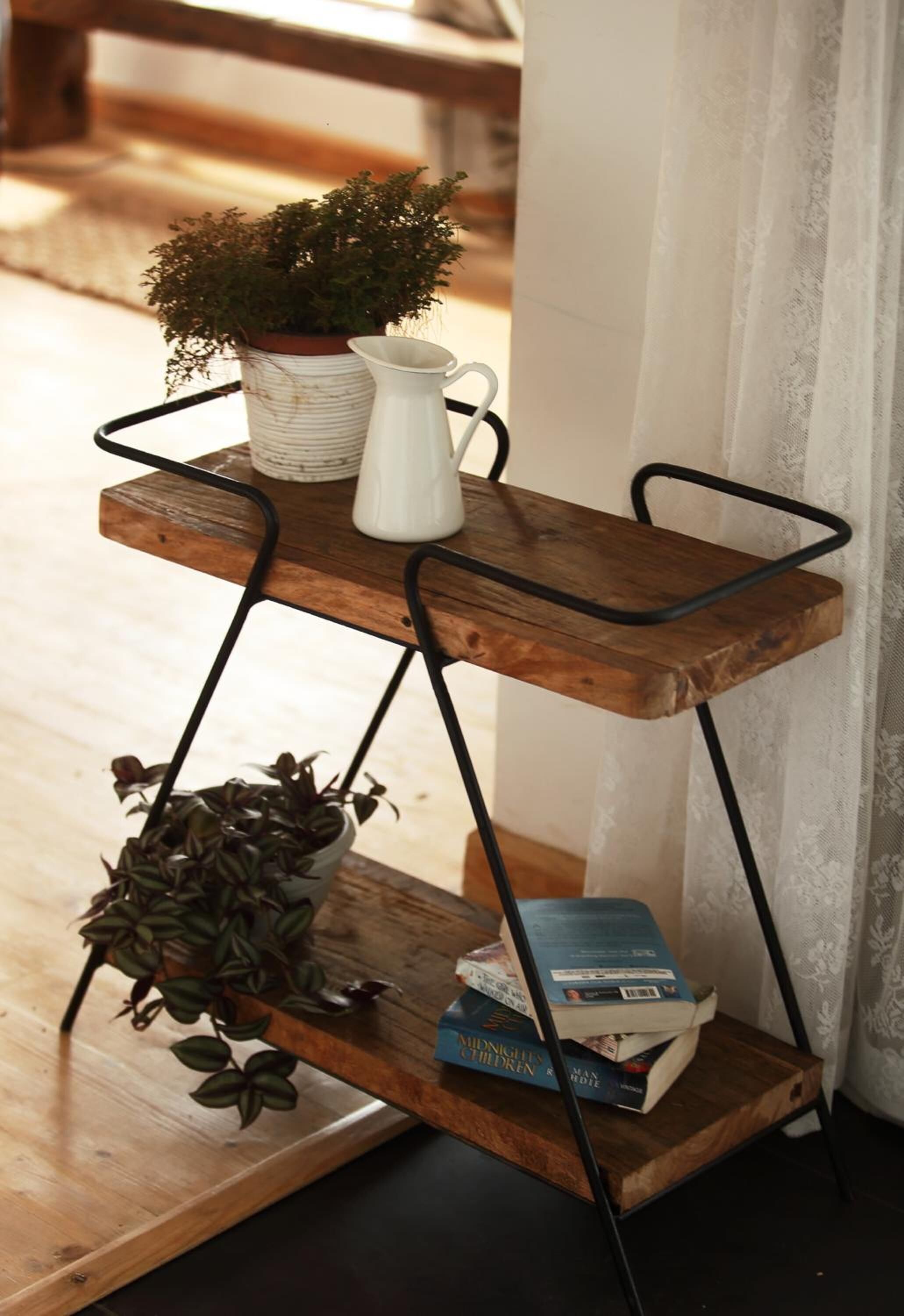 A wooden, metal-framed shelf with a potted plant, a white pitcher, and books.