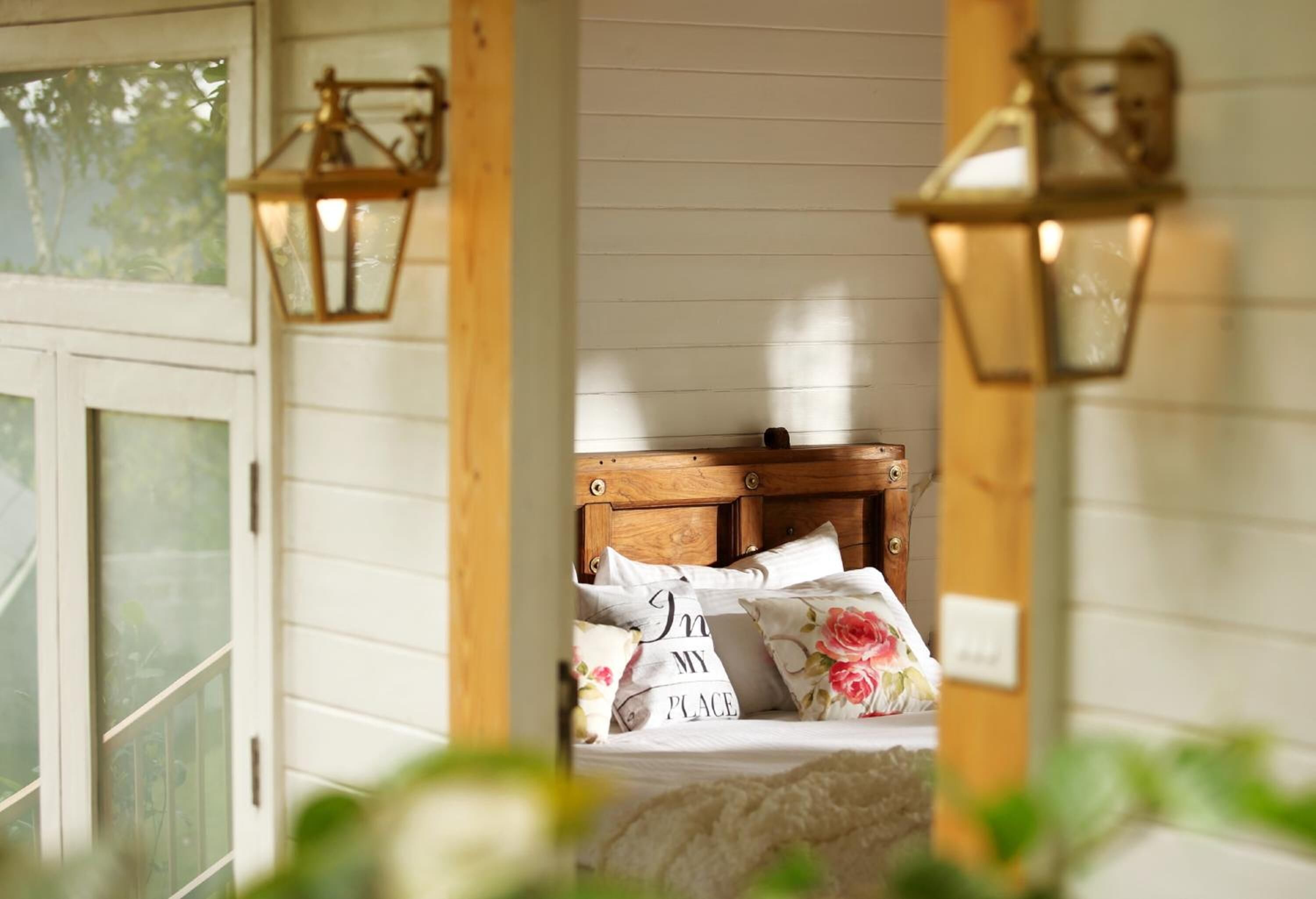 Un dormitorio con cabecera de madera, almohadas estampadas con motivos florales y ventana con vistas a zonas verdes.