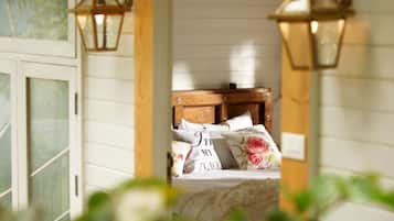 Un dormitorio con cabecera de madera, almohadas estampadas con motivos florales y ventana con vistas a zonas verdes.