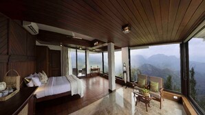 A bedroom with a large bed, a wooden ceiling, and a view of mountains through large windows. - Hills & Hues (Peermade)