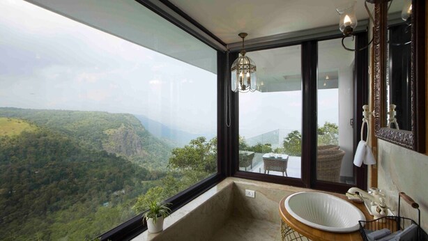 A bathroom with a large window offering a view of a mountainous landscape. - Hills & Hues (Peermade)