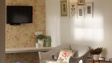 Um quarto acolhedor com uma cadeira de vime, uma pequena mesa branca e uma televisão de tela plana na parede.