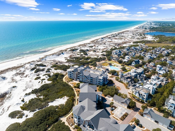An aerial view of a coastal residential area with houses, a beach, and a large building with a swimming pool.