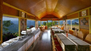 A dining area with long tables, chairs, and a view of the outdoors. - Vridhavan Mist City (Devikolam)