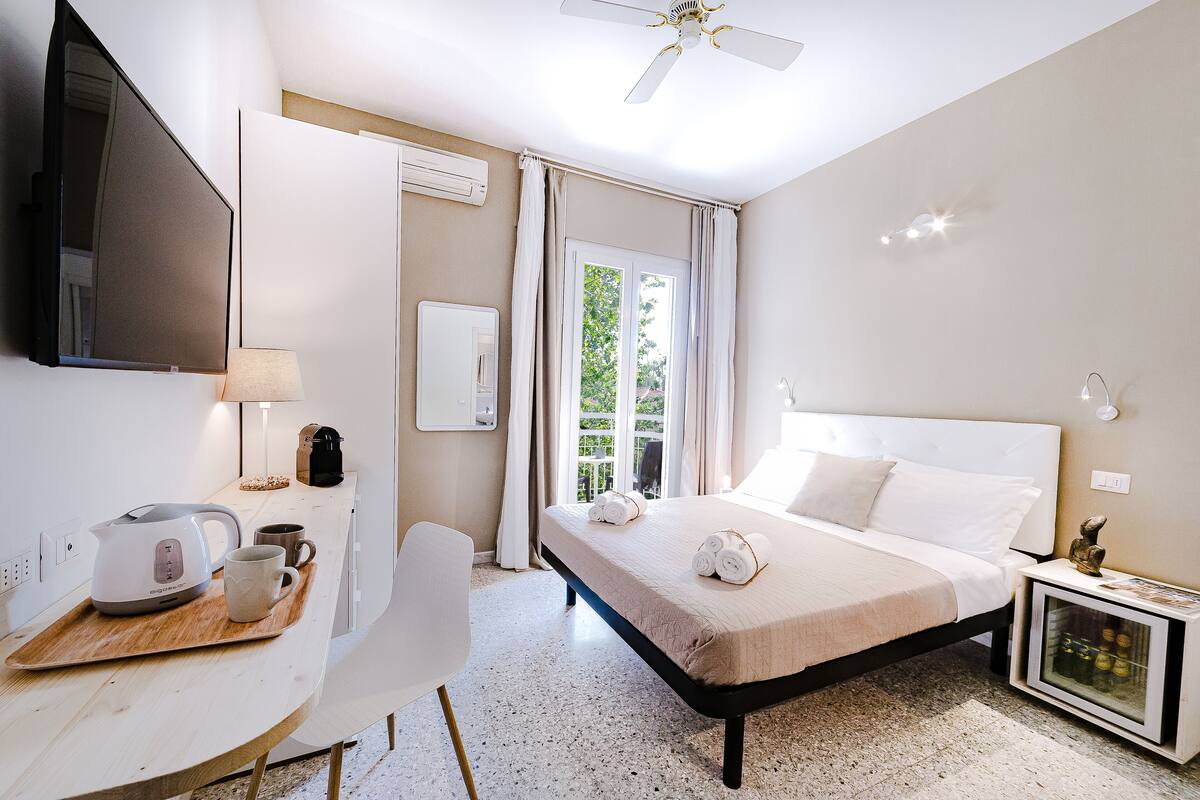 Une chambre d’hôtel équipée d’un lit, d’une table de chevet, d’une chaise et d’un bureau avec une bouilloire et une tasse.