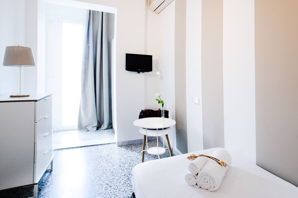 Une chambre d’hôtel avec un lit, un bureau, une chaise, une télévision et une fenêtre avec des rideaux.