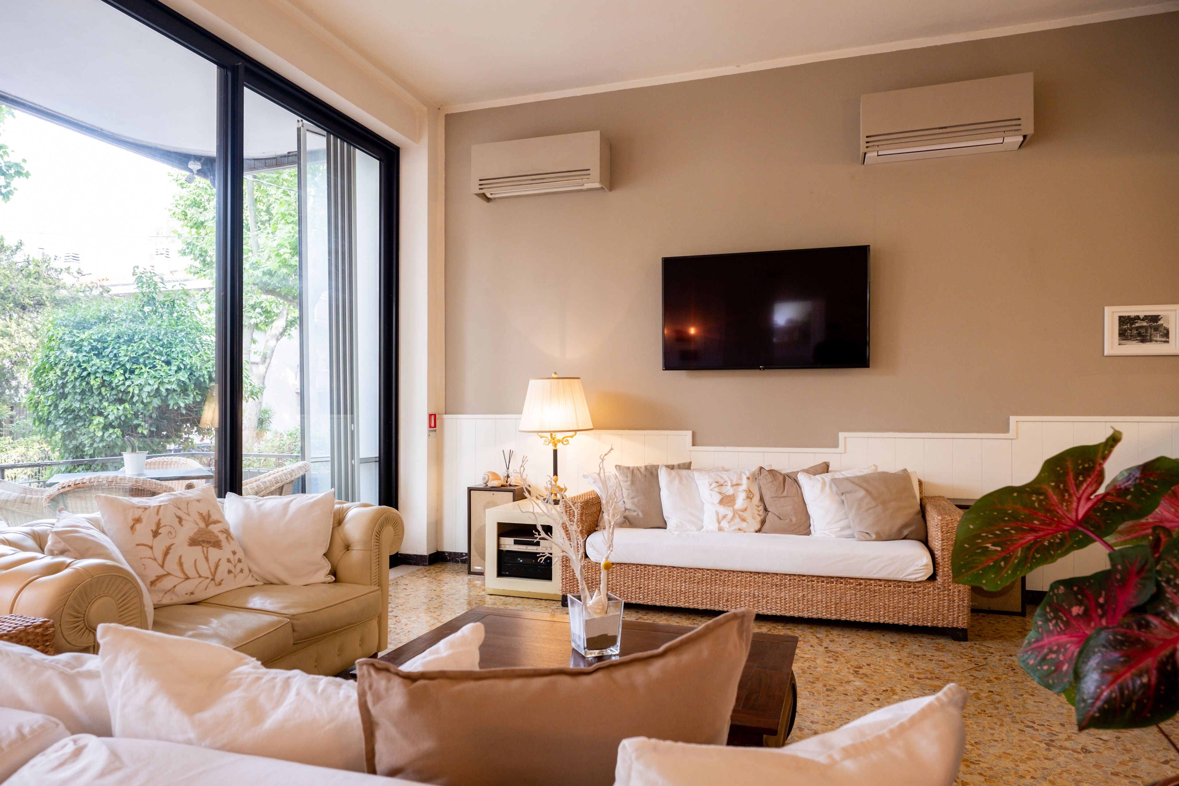 Ein Hotelzimmer mit großem Fenster, Flachbildfernseher, Sofa, Lampe und einer Pflanze.
