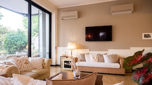 A hotel room with a large window, a flat-screen TV, a sofa, a lamp, and a plant. - De La Ville Boutique Hotel (Cattolica)