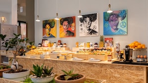 A breakfast bar with various food items and a coffee machine, surrounded by potted plants and artwork on the wall. - De La Ville Boutique Hotel (Cattolica)