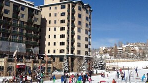A multi-story building with balconies, a ski resort in the background, and snow-covered trees. - Sheraton 3BR, 3BA: New Years Week- Top Fl. Direct on Mountain & 100% Ski-In/Out! (Steamboat Springs)