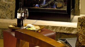 A stone fireplace with a modern TV screen, a bottle of wine, and glasses on a table in front of it. - Sheraton 3BR, 3BA: New Years Week- Top Fl. Direct on Mountain & 100% Ski-In/Out! (Steamboat Springs)
