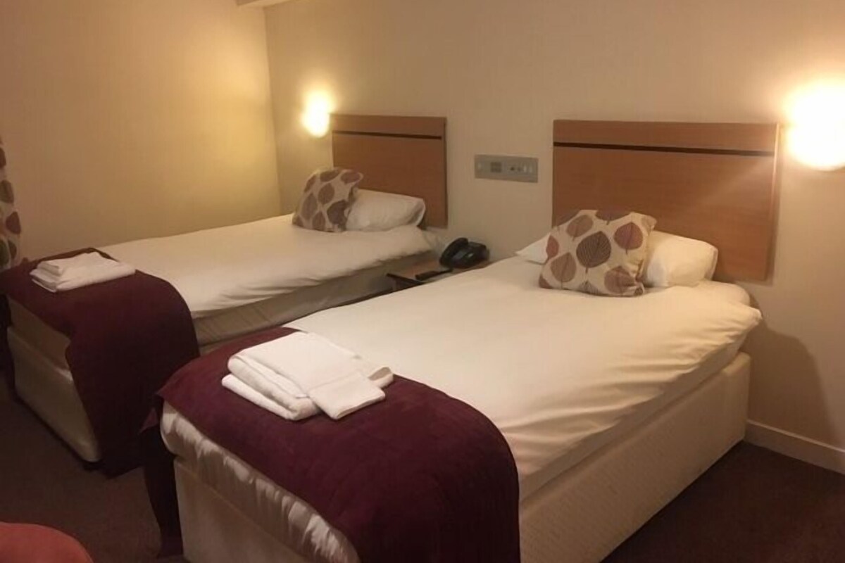 A hotel room with two single beds, each with a headboard, a bedside table, and a lamp.