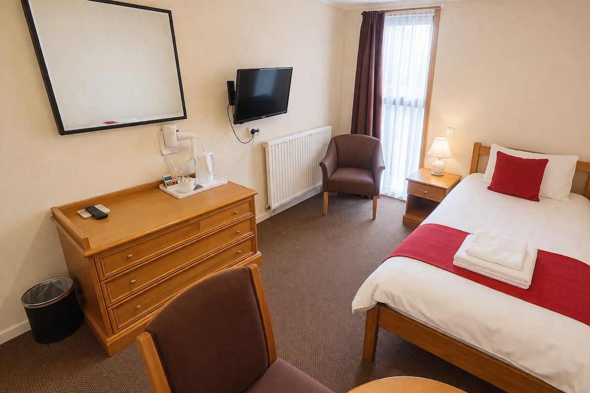 A hotel room with a bed, a desk, a chair, a TV, and a window with curtains.