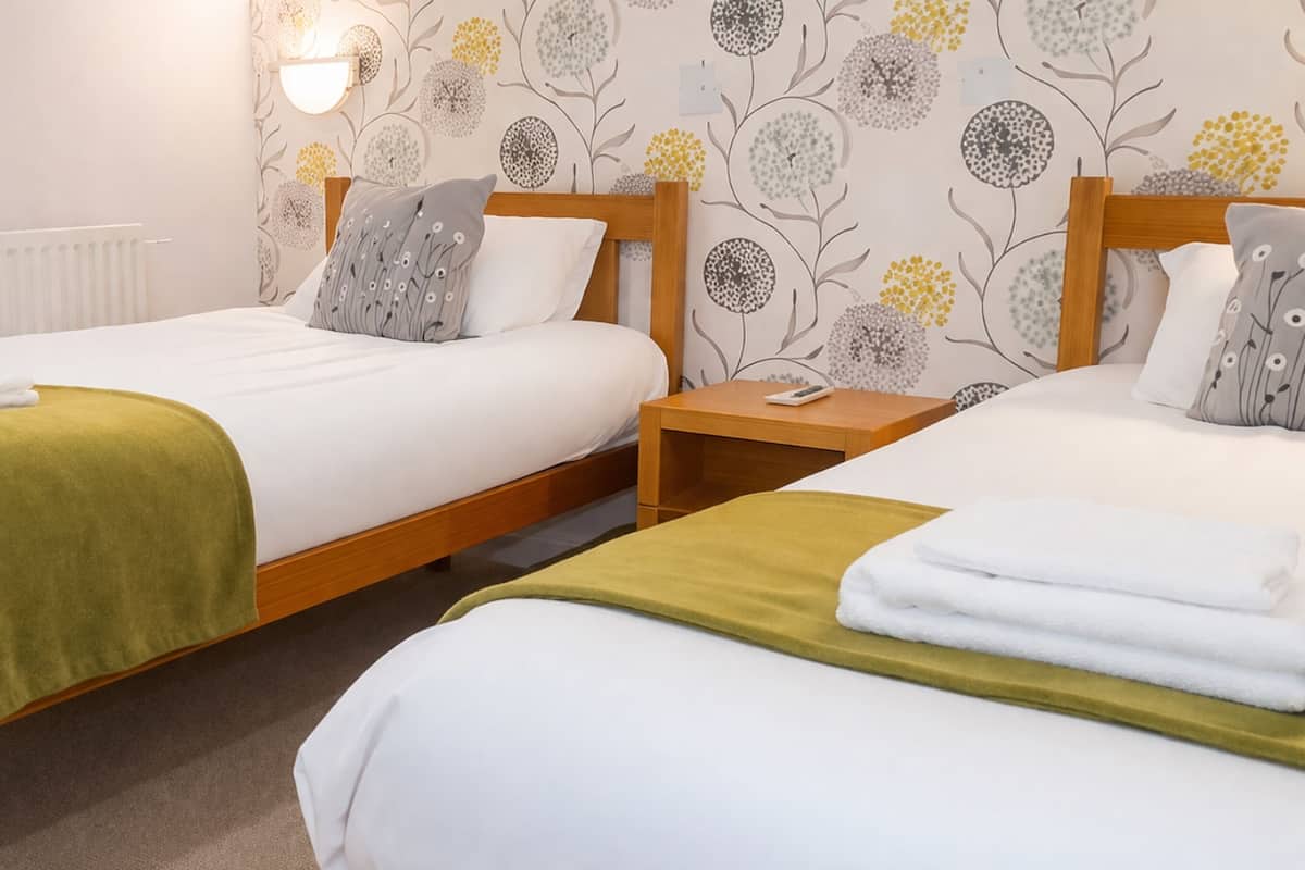 A double room with two beds, a bedside table, a mirror, and a radiator.