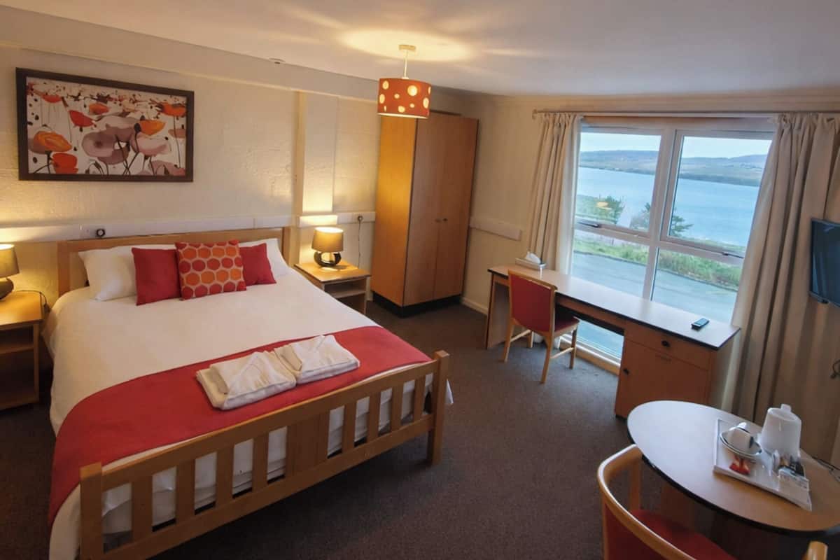 A hotel room with a bed, desk, chair, and a large window offering a view.