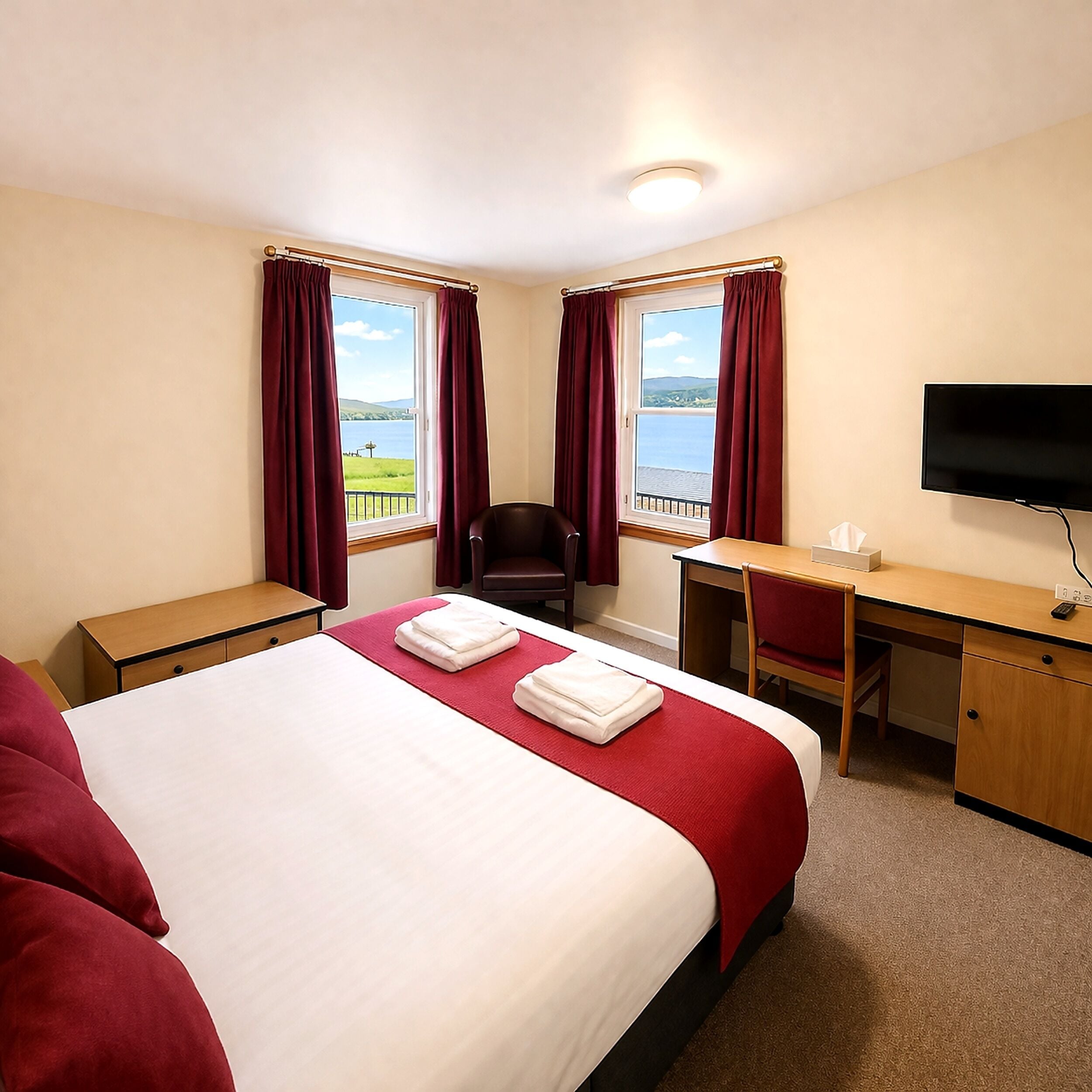 A hotel room with a bed, desk, chair, TV, and a window with curtains.