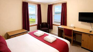A hotel room with a bed, desk, chair, TV, and a window with curtains.