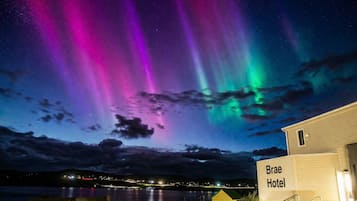 A hotel with a sign reading 'Brae Hotel' in front of a body of water, under a night sky with aurora borealis.
