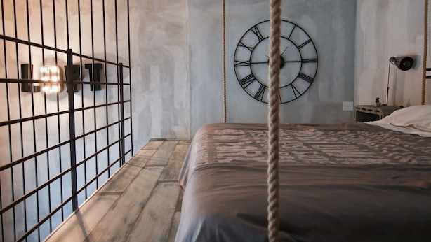 Un dormitorio con una cama, un reloj de pared, una cuerda y una reja de metal.